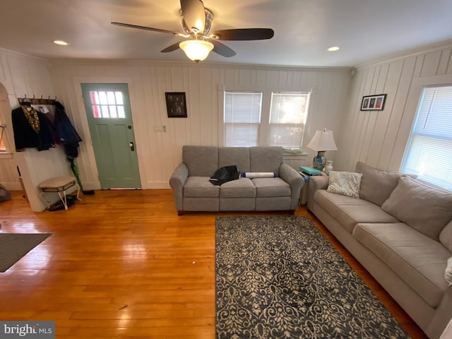 living room with light hardwood / wood-style flooring, ornamental molding, ceiling fan, and wood walls