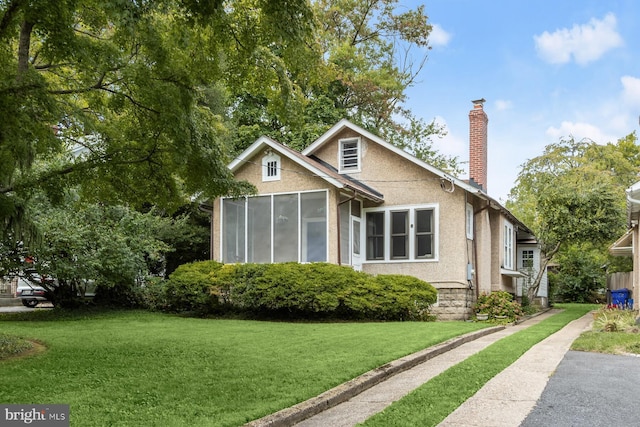 view of front of home with a sunroom, a chimney, a front lawn, and stucco siding