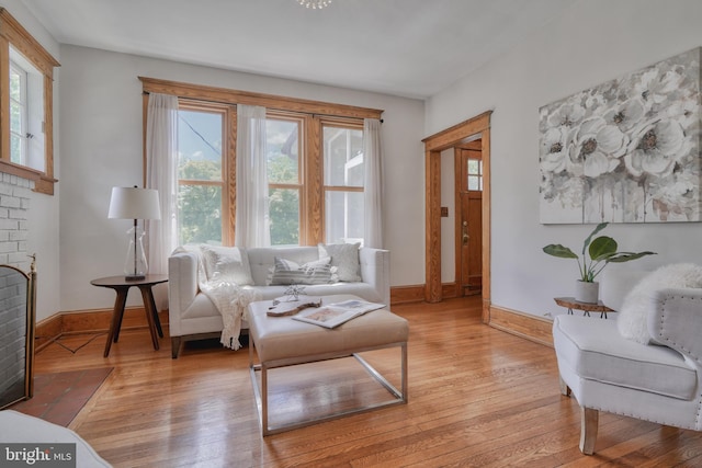 living area featuring a brick fireplace, light hardwood / wood-style flooring, and a healthy amount of sunlight