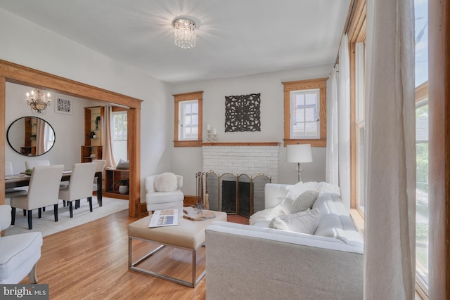 living room with a notable chandelier, a fireplace, light hardwood / wood-style floors, and a healthy amount of sunlight