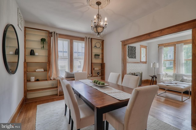 dining area with light wood-type flooring, a healthy amount of sunlight, baseboards, and an inviting chandelier