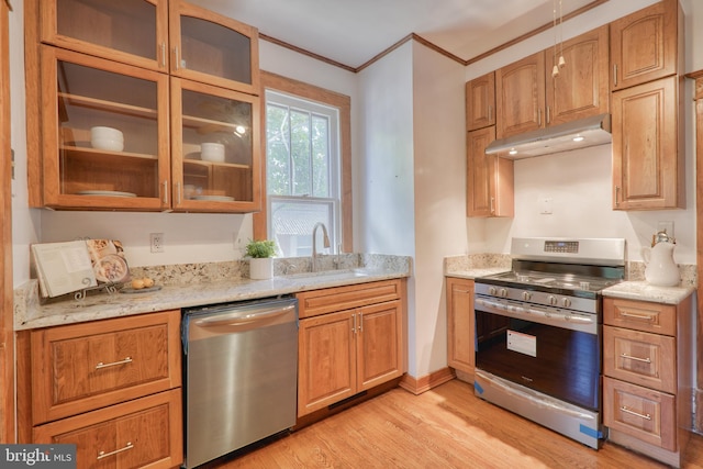 kitchen with light wood finished floors, glass insert cabinets, appliances with stainless steel finishes, under cabinet range hood, and a sink