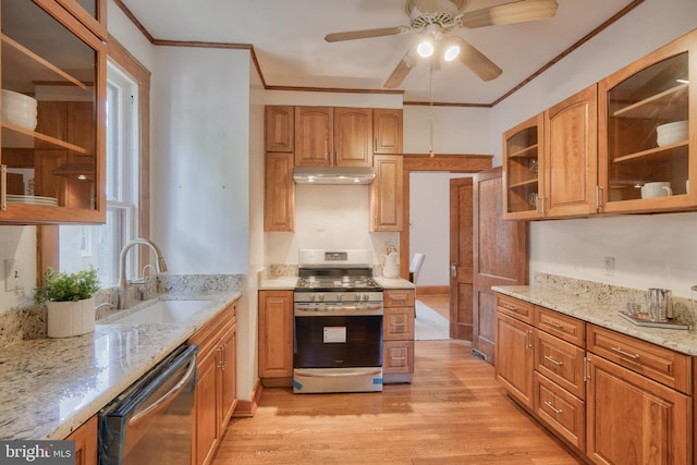 kitchen with light stone counters, appliances with stainless steel finishes, glass insert cabinets, a sink, and under cabinet range hood