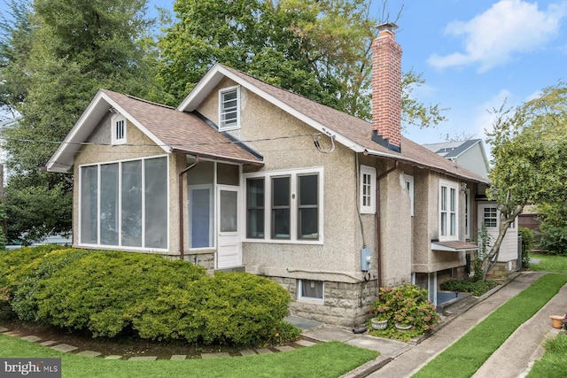 exterior space with a shingled roof, a sunroom, a chimney, and stucco siding