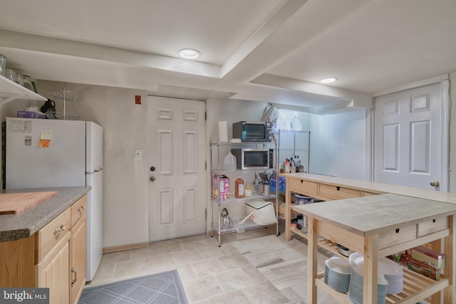 kitchen featuring stainless steel microwave, light brown cabinetry, and freestanding refrigerator