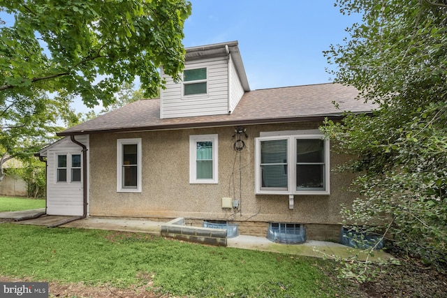 rear view of property featuring roof with shingles, a lawn, and stucco siding