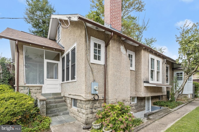 view of home's exterior with entry steps, a sunroom, a chimney, and stucco siding