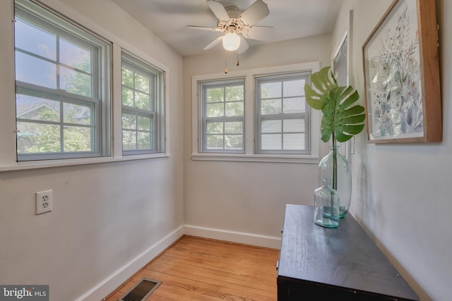 interior space with a ceiling fan, light wood-type flooring, visible vents, and baseboards