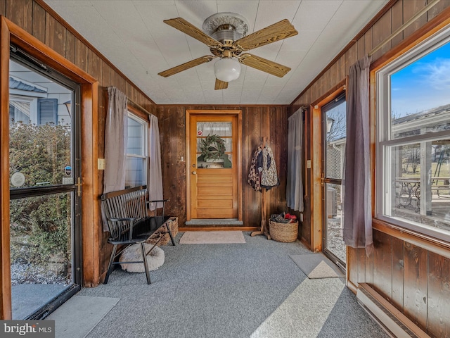 interior space with wood walls, ornamental molding, carpet floors, ceiling fan, and a baseboard heating unit