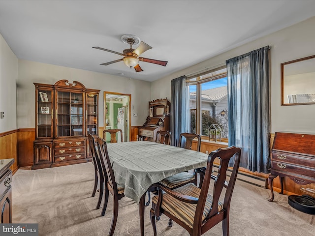 dining space with baseboard heating, light carpet, ceiling fan, and wood walls