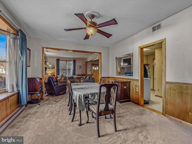 dining room with a baseboard radiator, light colored carpet, wooden walls, and ceiling fan