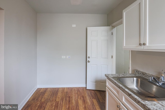 kitchen featuring baseboards, white cabinets, dark wood-type flooring, stone counters, and a sink