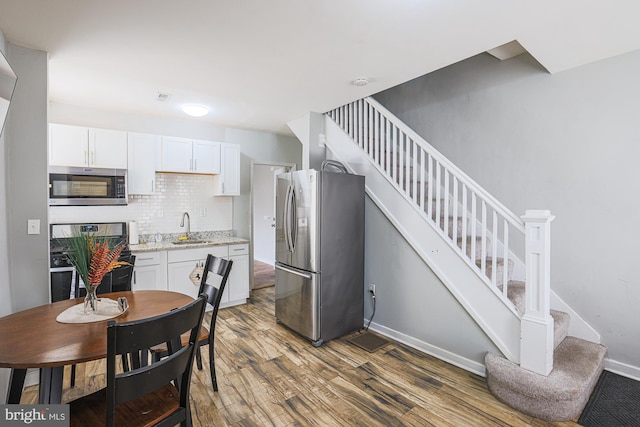 kitchen with stainless steel appliances, white cabinetry, a sink, and wood finished floors