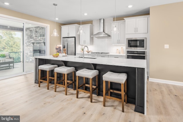 kitchen with appliances with stainless steel finishes, white cabinetry, hanging light fixtures, wall chimney exhaust hood, and a spacious island