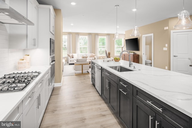 kitchen featuring white cabinetry, sink, hanging light fixtures, and wall chimney exhaust hood