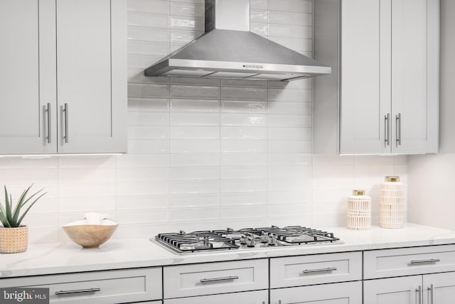 kitchen featuring gas stovetop, decorative backsplash, light stone counters, and wall chimney exhaust hood