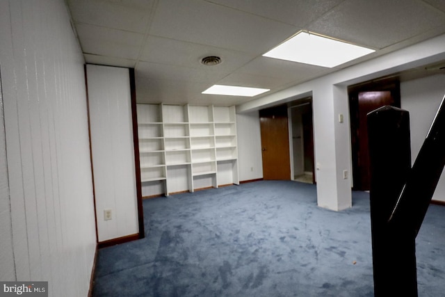 basement featuring dark carpet, built in features, and a drop ceiling