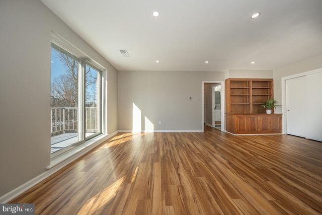 unfurnished living room featuring built in shelves and wood-type flooring