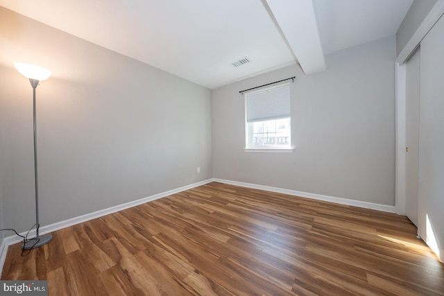 unfurnished bedroom with beamed ceiling and dark hardwood / wood-style flooring