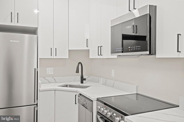 kitchen featuring stainless steel appliances, white cabinets, and light stone counters