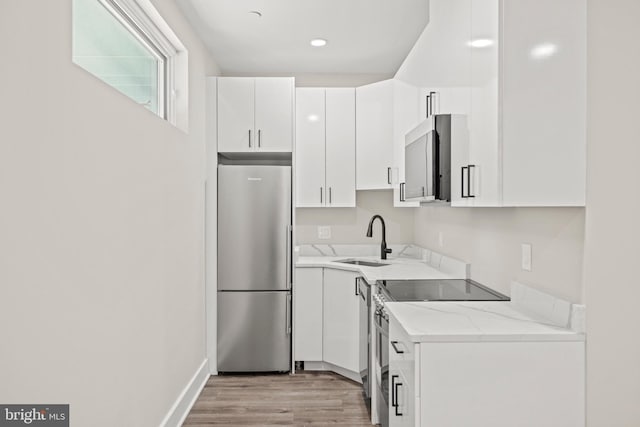 kitchen with sink, appliances with stainless steel finishes, white cabinetry, light stone countertops, and light wood-type flooring