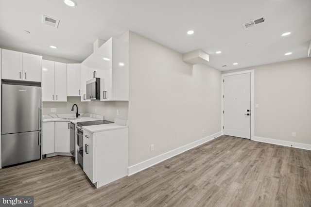 kitchen with appliances with stainless steel finishes, light hardwood / wood-style floors, sink, and white cabinets