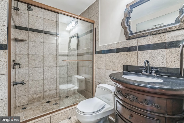 bathroom with tile walls, vanity, a shower with shower door, and toilet