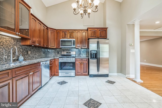 kitchen featuring dark stone countertops, a towering ceiling, decorative columns, and appliances with stainless steel finishes