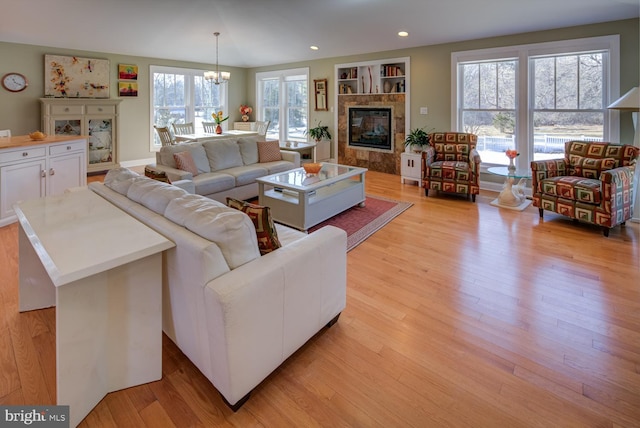 living room featuring built in features, a wealth of natural light, a tile fireplace, and a chandelier