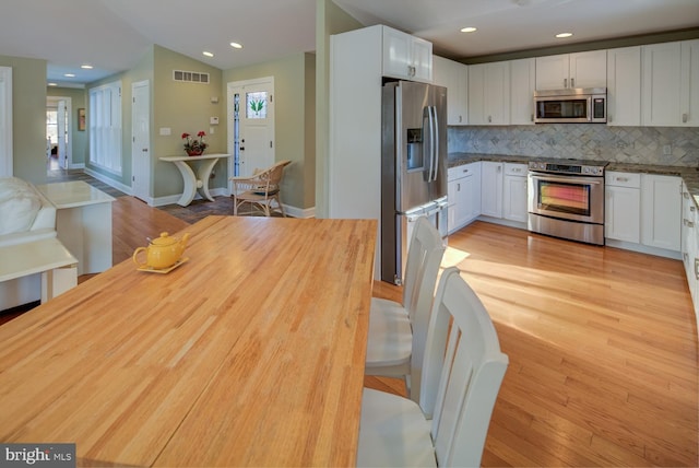 kitchen with light hardwood / wood-style flooring, white cabinetry, stainless steel appliances, tasteful backsplash, and vaulted ceiling