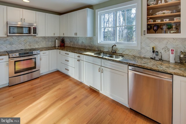 kitchen with sink, light wood-type flooring, stone counters, stainless steel appliances, and white cabinets