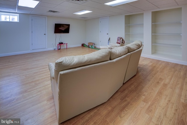 living room with a drop ceiling, built in features, and light wood-type flooring