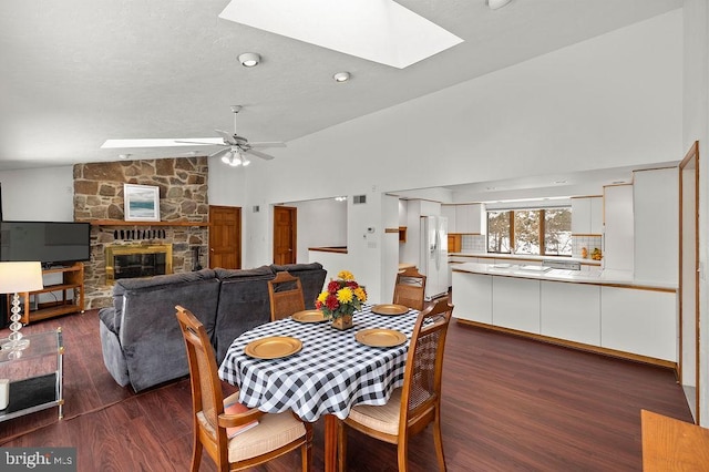 dining area featuring lofted ceiling with skylight, dark hardwood / wood-style floors, ceiling fan, and a fireplace