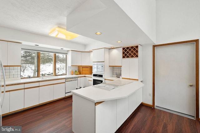 kitchen with white cabinetry, tasteful backsplash, dark hardwood / wood-style flooring, kitchen peninsula, and white appliances