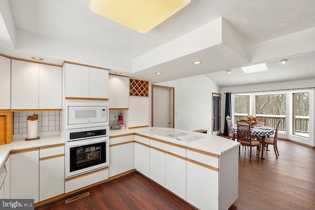 kitchen featuring dark hardwood / wood-style floors, tasteful backsplash, white cabinetry, kitchen peninsula, and white appliances