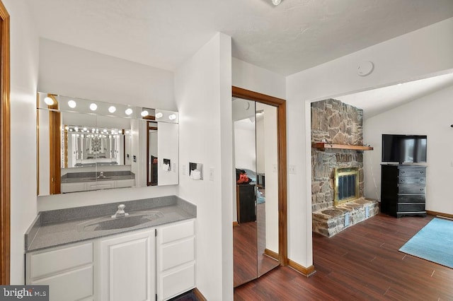 bathroom featuring vanity, vaulted ceiling, wood-type flooring, and a fireplace