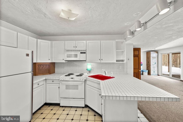 kitchen with sink, tile counters, kitchen peninsula, white appliances, and white cabinets