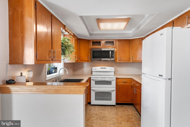 kitchen with sink, kitchen peninsula, white appliances, and a tray ceiling