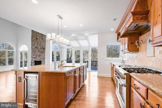 kitchen with lofted ceiling, wine cooler, stainless steel range, a center island with sink, and decorative light fixtures