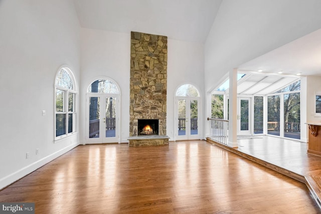 unfurnished living room with french doors, a stone fireplace, high vaulted ceiling, and hardwood / wood-style flooring