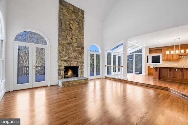 unfurnished living room with french doors, a stone fireplace, high vaulted ceiling, and light hardwood / wood-style flooring