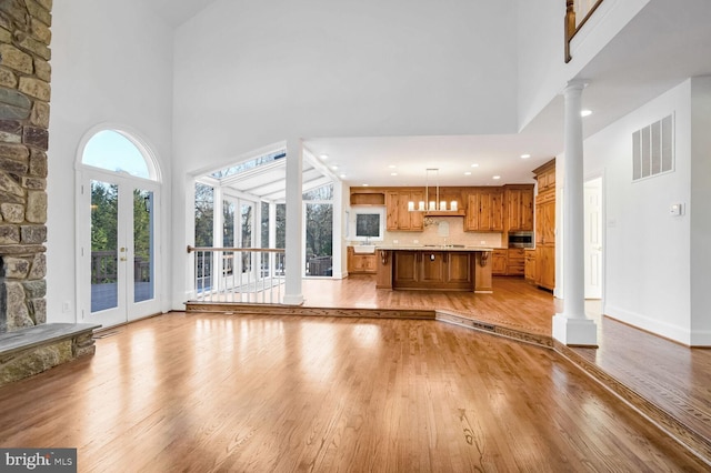 unfurnished living room with sink, light hardwood / wood-style floors, a high ceiling, and ornate columns