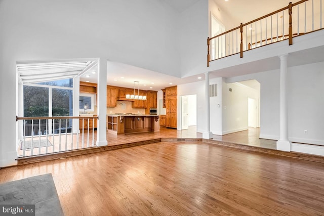 unfurnished living room featuring light wood-type flooring, high vaulted ceiling, and ornate columns