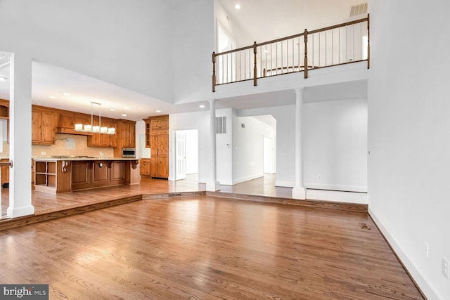 unfurnished living room with a towering ceiling, light hardwood / wood-style floors, and ornate columns