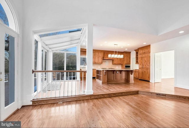 kitchen featuring decorative light fixtures, lofted ceiling, decorative backsplash, stainless steel appliances, and light hardwood / wood-style flooring