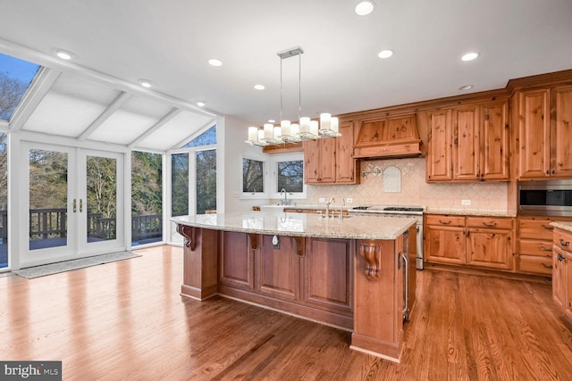 kitchen with premium range hood, vaulted ceiling with beams, decorative light fixtures, appliances with stainless steel finishes, and a kitchen island with sink