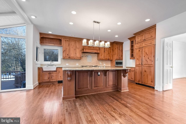 kitchen with hardwood / wood-style floors, stainless steel microwave, an island with sink, sink, and hanging light fixtures