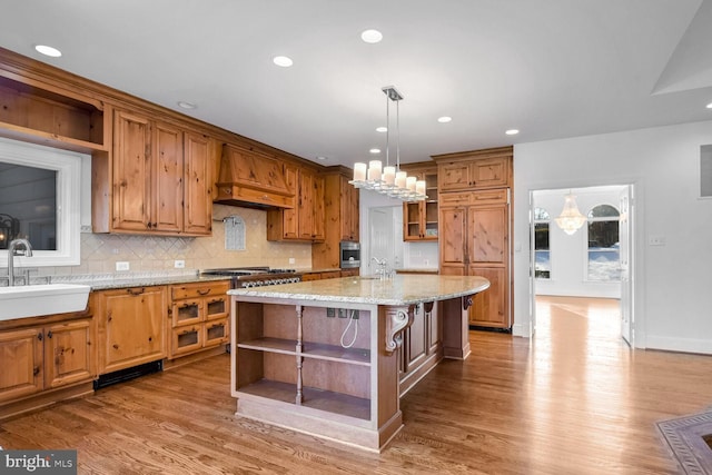 kitchen with premium range hood, sink, a center island, hanging light fixtures, and light hardwood / wood-style floors