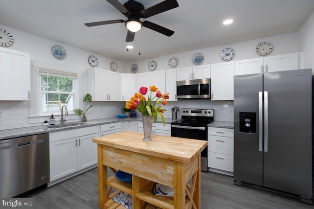 kitchen with appliances with stainless steel finishes, white cabinetry, sink, dark hardwood / wood-style flooring, and light stone countertops