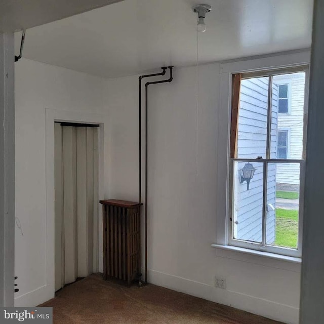 spare room featuring carpet floors, radiator, and plenty of natural light